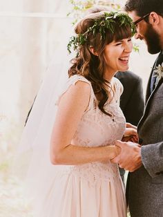 a bride and groom smile at each other as they stand under an arch with greenery on it