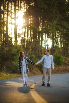 a man and woman holding hands while walking down the road in front of some trees