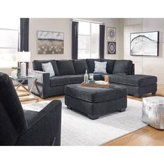 a living room with gray furniture and white rugs on the floor, windows in the background