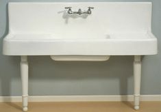 a white sink sitting on top of a wooden floor next to a wall mounted faucet