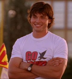 a man with his arms crossed standing in front of two flags and smiling at the camera