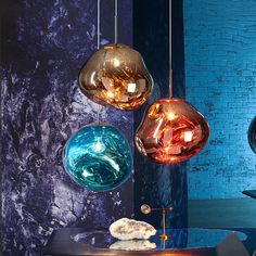 three different colored glass balls hanging from a blue brick wall next to a black table