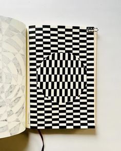 an open book with black and white designs on it next to a light bulb that is plugged in