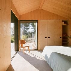 a bedroom with wooden walls and flooring has a white bed in the corner, along with a chair