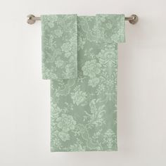 two green floral towels hanging on a towel rack in front of a white bathroom wall