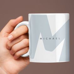 a hand holding a coffee mug with michael on the front and side, against a brown background