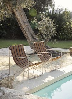 two lounge chairs sitting next to a tree near a swimming pool in a backyard area