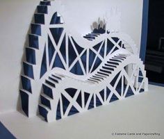 a paper sculpture of a piano on a white table with blue and white walls in the background