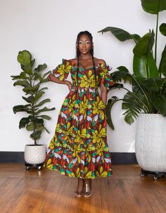 a woman standing in front of some plants wearing a colorful dress with flowers on it