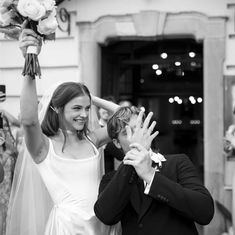 a man and woman standing next to each other in front of a building with flowers