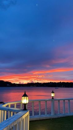 the sun is setting over the water and there are two lights on the railings