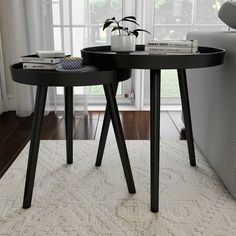 two black tables sitting on top of a white rug in front of a couch and window