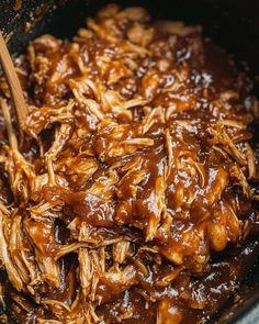 shredded meat and sauce in a skillet with wooden spoons