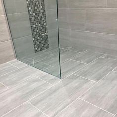 a glass shower door in a bathroom with grey tile on the walls and flooring