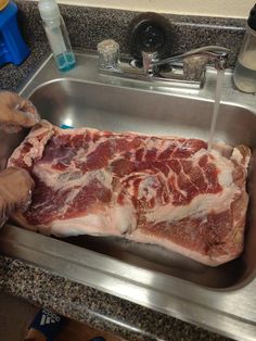 a person washing meat in a kitchen sink