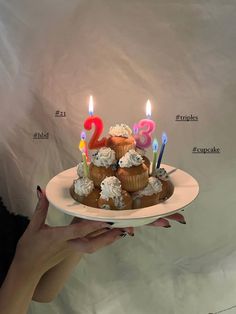 a woman holding a plate with cupcakes and candles on it