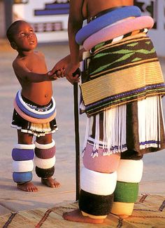 a young boy standing next to an african man holding a stick and wearing colorful clothing