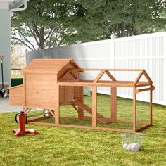 a wooden chicken coop in the grass next to a white fence