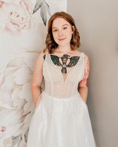 a woman standing in front of a floral wallpaper wearing a white dress and black bow tie