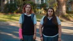 two young women standing next to each other on the side of a road with trees in the background