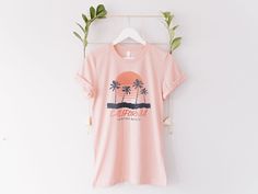 About Design- California Palm Tree Sunset Beach Surfing T-shirt - Beach Vibes California State Retro Vintage Design Printed Tee Shirt.- Design placement on the actual product can be slightly different than on the photo shown depending on the size and other conditions. About T-Shirt- These premium T-shirts are made with a modern "Side Seamed" body design and it provides a superior fit compared to the old-schooled "Tubular body T-shirt" which looks so baggy and cheap.Material- 52% pre-shrunk ring- Cheap Palm Tree Print Tops For Beach, Pink Cotton Top With Palm Tree Print, Pink Palm Tree Print Short Sleeve Top, Spring Crew Neck T-shirt With Palm Tree Print, Pink Tropical T-shirt For Summer, Spring Palm Tree Print Short Sleeve T-shirt, Casual Palm Tree Print T-shirt For Spring, Pink Relaxed Fit T-shirt For Surfing, Pre-shrunk Pink Tops For Beach Season