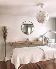 a white bed sitting under a round mirror in a bedroom next to a wooden floor