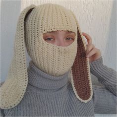 a woman wearing a knitted hat and scarf covering her face with a bunny ear