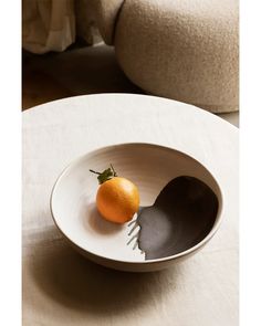 an orange sitting in a white bowl on top of a table