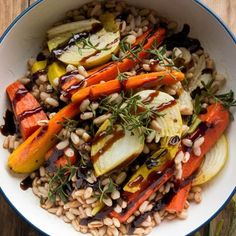 a white bowl filled with carrots, beans and fennel on top of a wooden table