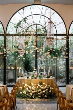 an indoor dining area with chandeliers and flowers on the table in front of large windows