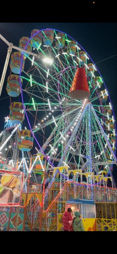 an amusement park at night with people standing around the ferris wheel and lights on it