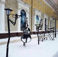 several metal sculptures on the side of a building covered in snow and light poles with lights attached to them