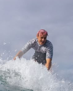 a woman with pink hair riding a surfboard in the ocean