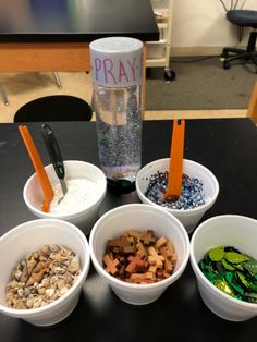 four bowls filled with different types of rocks on a table next to a glass bottle