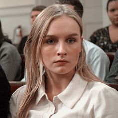 a woman with long hair sitting in a chair looking at the camera while others look on