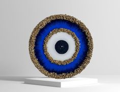 a blue and gold object on a white pedestal with a black dot in the center