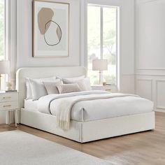 a white bed sitting in a bedroom on top of a hard wood floor next to two windows