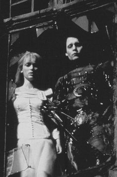 a man and woman standing next to each other in front of a window with an alien costume on