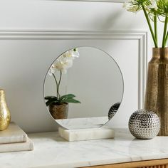 a mirror sitting on top of a table next to a vase with flowers in it