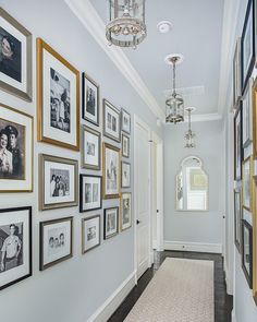 a hallway with many framed pictures on the wall and a chandelier hanging from the ceiling