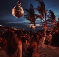 a group of people standing next to each other on a beach at night with disco balls hanging from palm trees