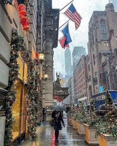 a woman walking down a street in the rain with an umbrella and american flags hanging from buildings