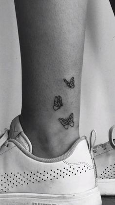 a black and white photo of a woman's foot with three butterflies on it