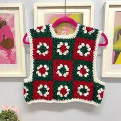 a green and red crocheted sweater hanging from a hook on a wall next to pictures