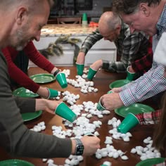 three men and one woman are playing with small white snowballs on the table in front of them