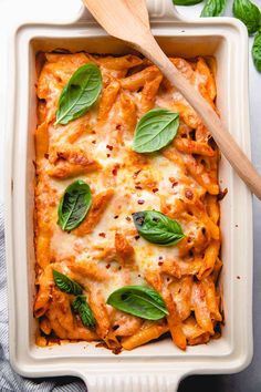 a casserole dish filled with pasta and spinach leaves, topped with parmesan cheese