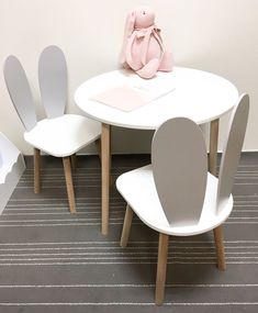 a white table with four chairs and a pink teddy bear on the chair next to it