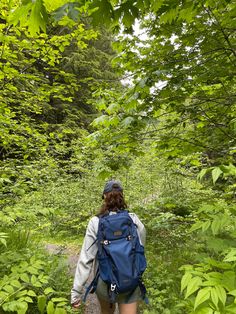 a woman with a blue backpack is walking through the woods