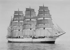 a black and white photo of a large sailboat in the ocean with sails down