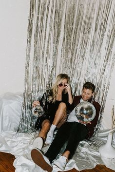 a man and woman sitting on top of a bed next to each other holding disco balls